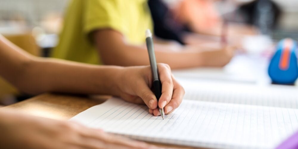 Close up of left handed school child writing in notebook.